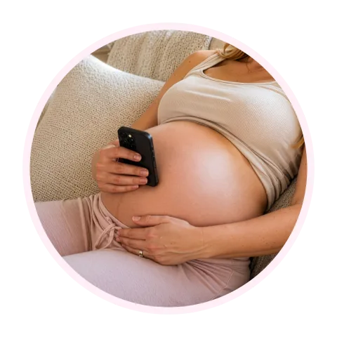 A pregnant woman lying on a sofa, holding her phone flat against her bump